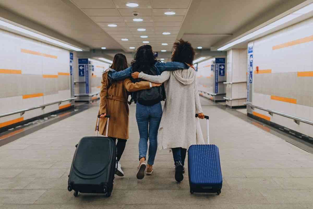 Amiche abbracciate che camminano in aeroporto trascinando il bagaglio a mano