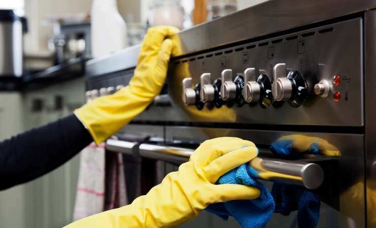 Mani ricoperte da guanti gialli che puliscono il forno.