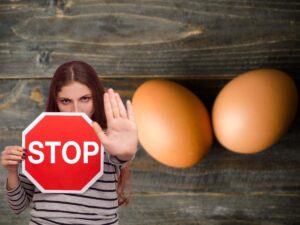 uova su tavolo di legno e donna con cartello di stop