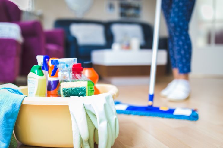 donna che pulisce il pavimento e kit di pulizie in evidenza