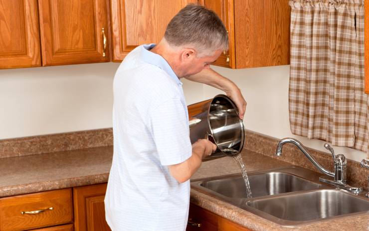 uomo versa acqua da pentola nel lavandino