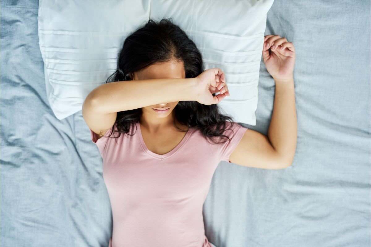 Ragazza con braccio sul viso nel letto