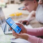 Ragazza con smartphone prenotazione aereo, di fianco a lei ragazzo al pc