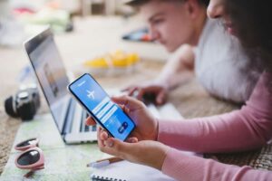 Ragazza con smartphone prenotazione aereo, di fianco a lei ragazzo al pc